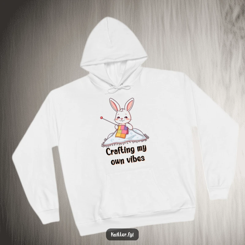 Funny hoodie showing a happy rabbit character meticulously sewing a colorful patch onto a blanket, radiating crafting enthusiasm.