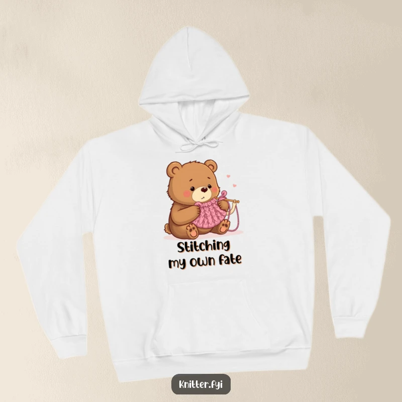 Funny hoodie depicting a focused bear humorously knitting a small tea cozy with comically large needles, ideal for cold days.
